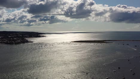 Aerial-drone-shot-from-left-to-right,-showing-Dawlish-Warren-Spit,-the-Exe-Estuary-and-Exmouth,-with-shimmering-light-in-Devon-,-UK