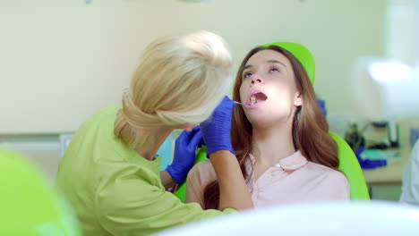 Dentist-examining-patient-teeth-with-mouth-mirror.-Stomatologist-and-patient