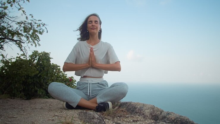 Chica feliz y sana con las palmas juntas sentada en una roca de montaña con vistas al mar.