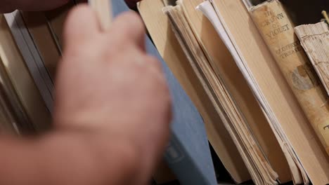 Close-up-of-a-person-removing-a-blue-hardcover-book-from-a-shelf-and-then-putting-it-back