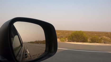 conduciendo por una carretera del desierto mientras mira en el espejo retrovisor lateral del camión