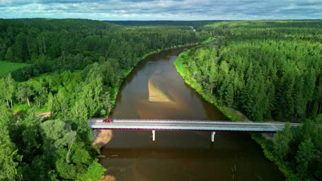 aerial view of vehicle parked over bridge in river stream surrounded by coniferous tree forest