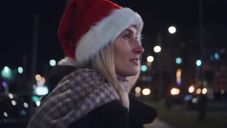 a beautiful woman in a santa claus hat walks at night on christmas