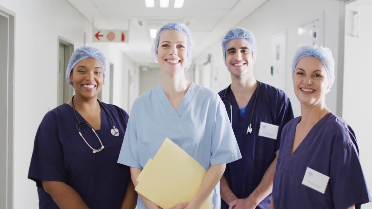 retrato en video de un grupo diverso de trabajadores médicos con gorras quirúrgicas sonriendo en el pasillo del hospital.