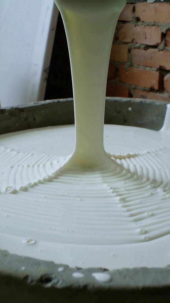 Vertical video: Opening top pipe pouring thick white liquid filling basin in workshop for mold