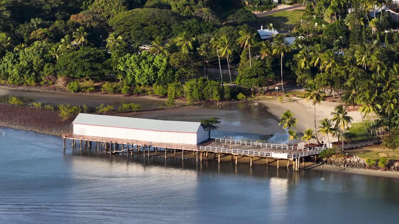 Drone captures serene tropical landscape with a pier, lush greenery, and calm waters in Port Douglas, Australia