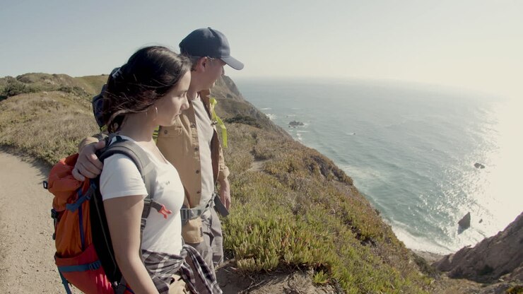 Padre e hija haciendo senderismo en la cima de la montaña, de pie en un acantilado y disfrutando de la vista al mar.