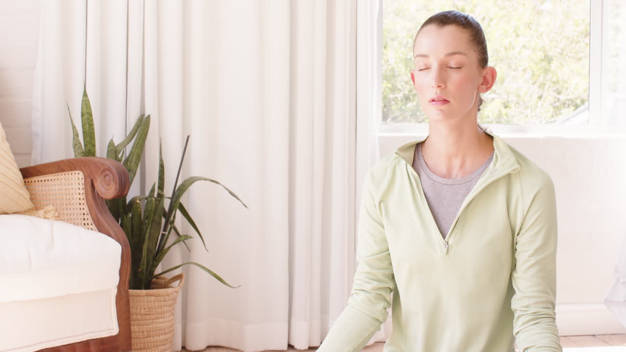 Woman meditating at home, sitting peacefully with closed eyes near window