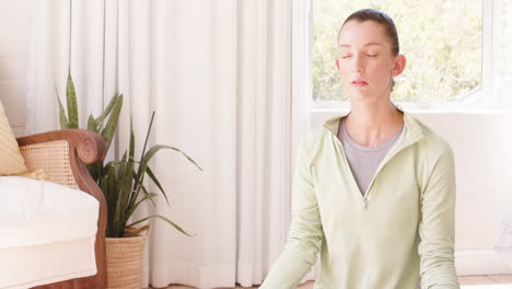 woman meditating at home, sitting peacefully with closed eyes near window