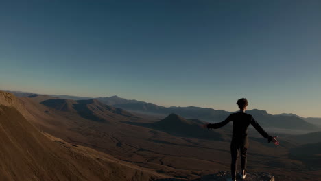 A person stands on a mountain peak admiring the vast landscape at sunrise or sunset