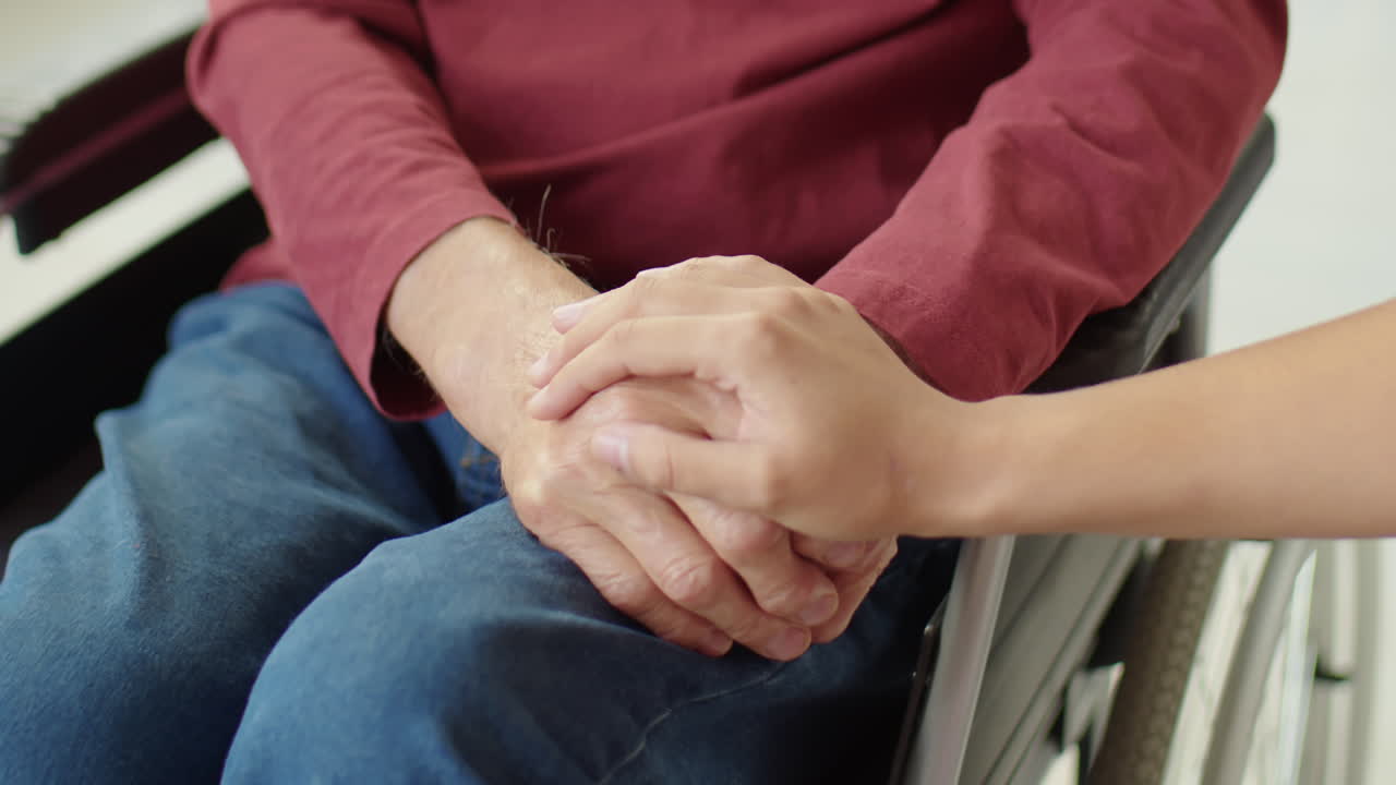 Woman Holding Hands of Senior Man in Wheelchair