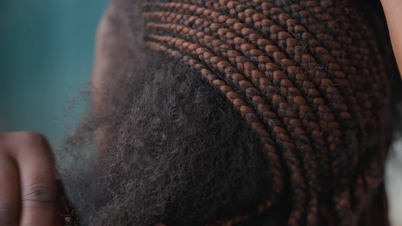 Primo piano che rivela la texture dei capelli di una donna di colore, corona intrecciata in contrasto con una sezione afro naturale, profilo laterale con una mano delicata vicino al cuoio capelluto, sfondo turchese calmo, momento autentico in salone che mette in risalto