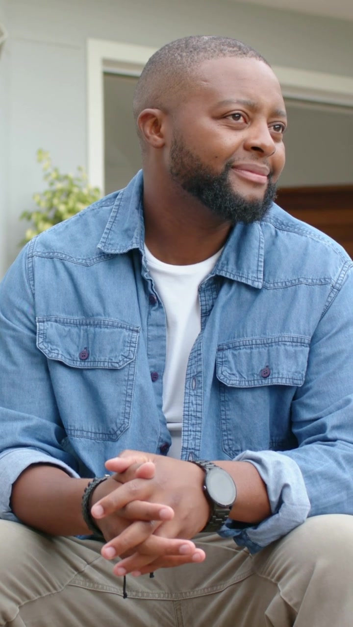 Video verticale: Uomo seduto in denim che sposta lo sguardo a destra su un gradino, sorridendo e mostrando l'orologio