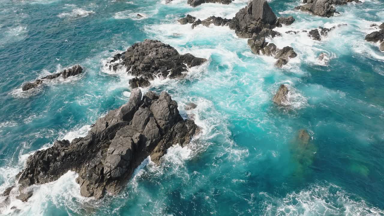 el dron vuela cerca de las escasas rocas del acantilado aplastadas por las olas en el mar azul japonés cristalino