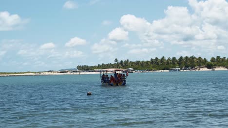 A-full-transport-boat-full-of-locals-and-tourists-leaving-the-Barra-de-Cunhaú-beach-and-sailing-towards-the-Restinga-beach-in-Canguaretama-in-Rio-Grande-do-Norte,-Brazil-on-a-warm-sunny-summer-day