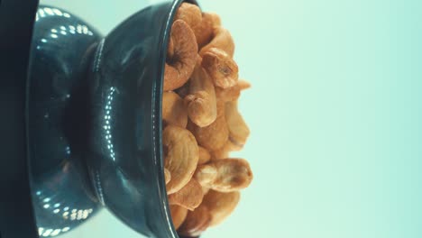 a vertical close up shot of a roasted salty cashew in a black shiny bawl on a rotating stand, slow motion, 4k