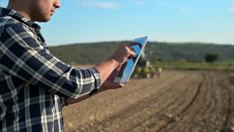 agricultor con tableta digital en un fondo de tractor arando en el campo. concepto de agricultura inteligente. imágenes de alta calidad 4k