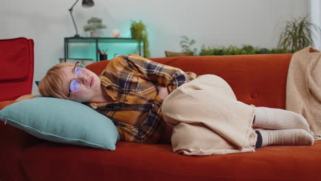 sick ill woman suffering from period cramps stomach ache menstrual pain lying on sofa at home room