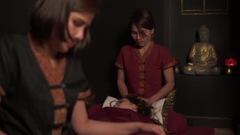 dos terapeutas tailandesas haciendo masaje para una mujer en un salón de spa. masaje tailandés de dos manos de piernas y cabeza. toma de 4k