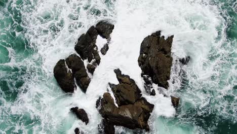 static aerial top down of heavy waves crashing against rock formation in ocean, riversdale, new zealand