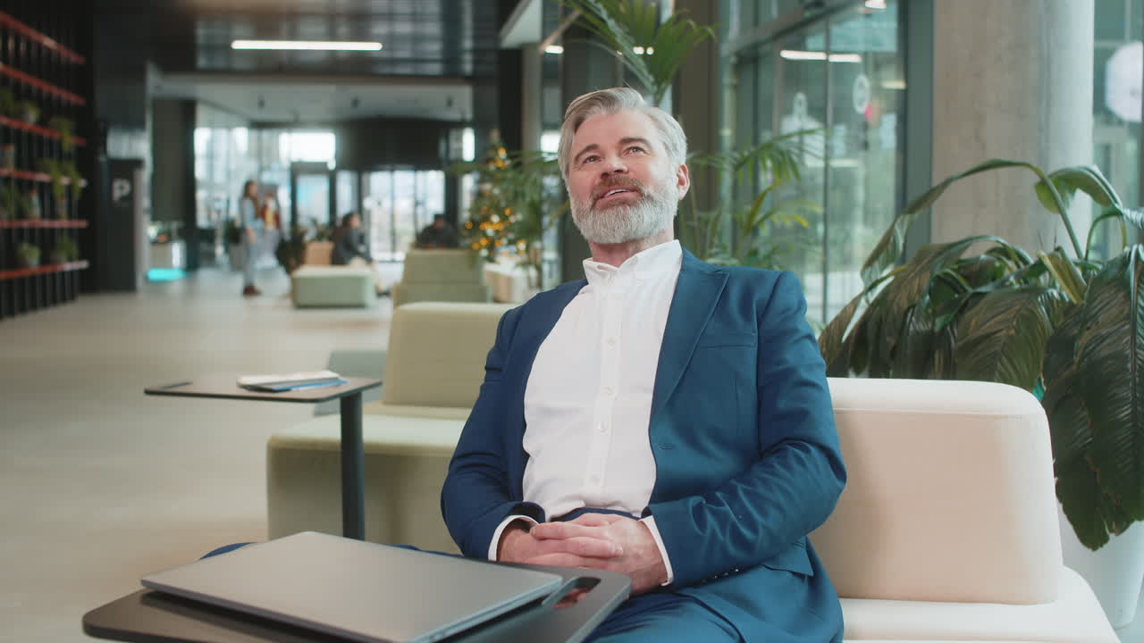 Happy businessman sitting in office lobby closing laptop and stretching arms after finishing work