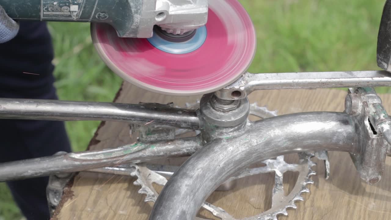 Worker grinding metal with a metal grinding machine. Repairing an old bike