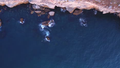 vista aerea dall'alto verso il basso delle onde che si tuffano contro la spiaggia rocciosa, sfondo