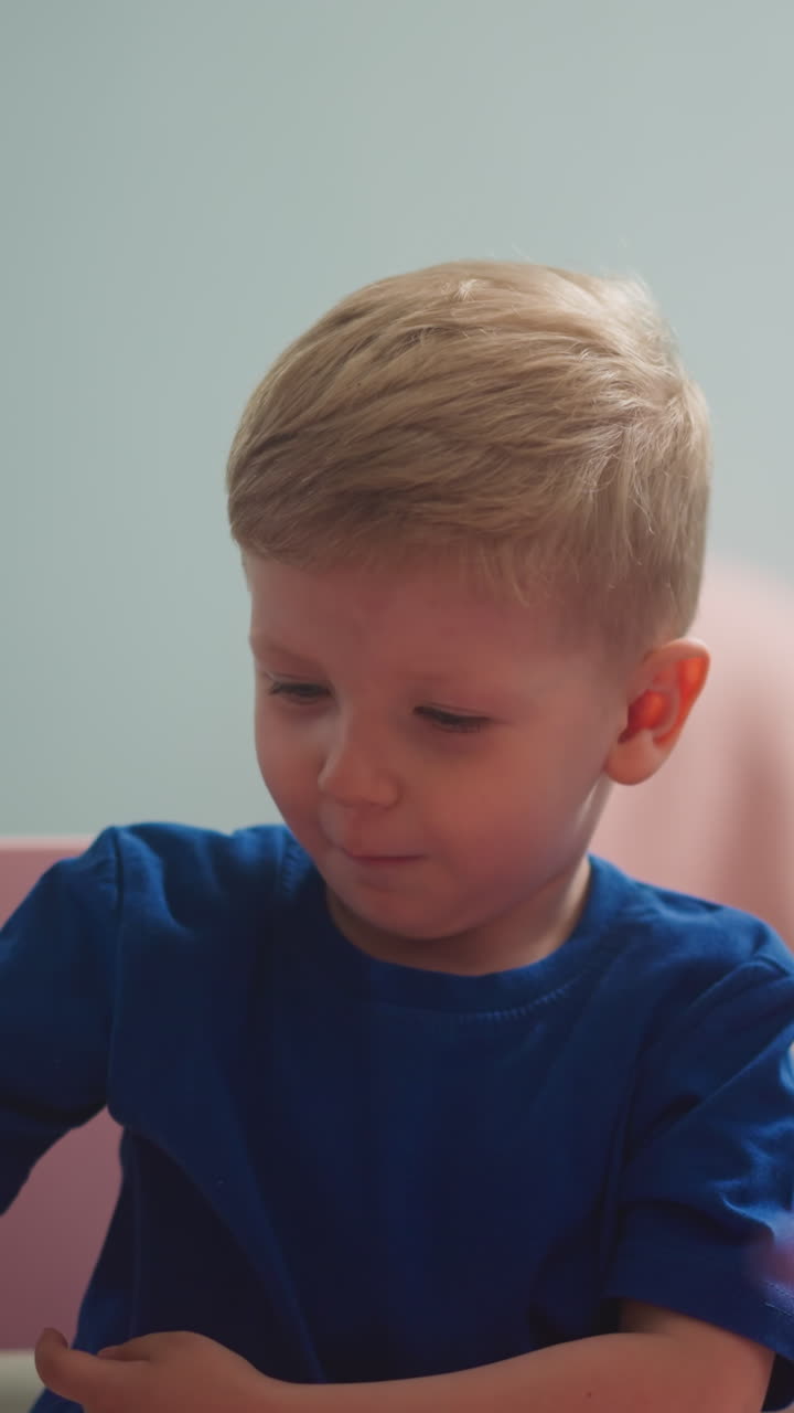 Smiling little boy inserts stick into soil and gets disgusting of dirt at home closeup slow motion. Toddler throws stick sitting with sister at table