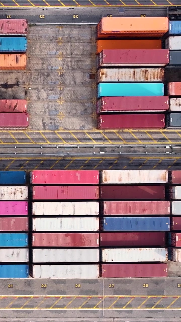 Pemandangan udara terminal peti kemas yang sibuk, menunjukkan peti kemas tersusun rapi. Peralatan derek memuat peti kemas ke kapal kargo untuk perdagangan internasional
