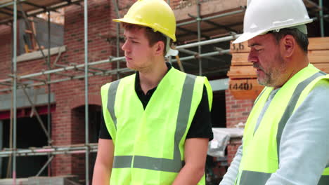 builder on building site discussing work with apprentice