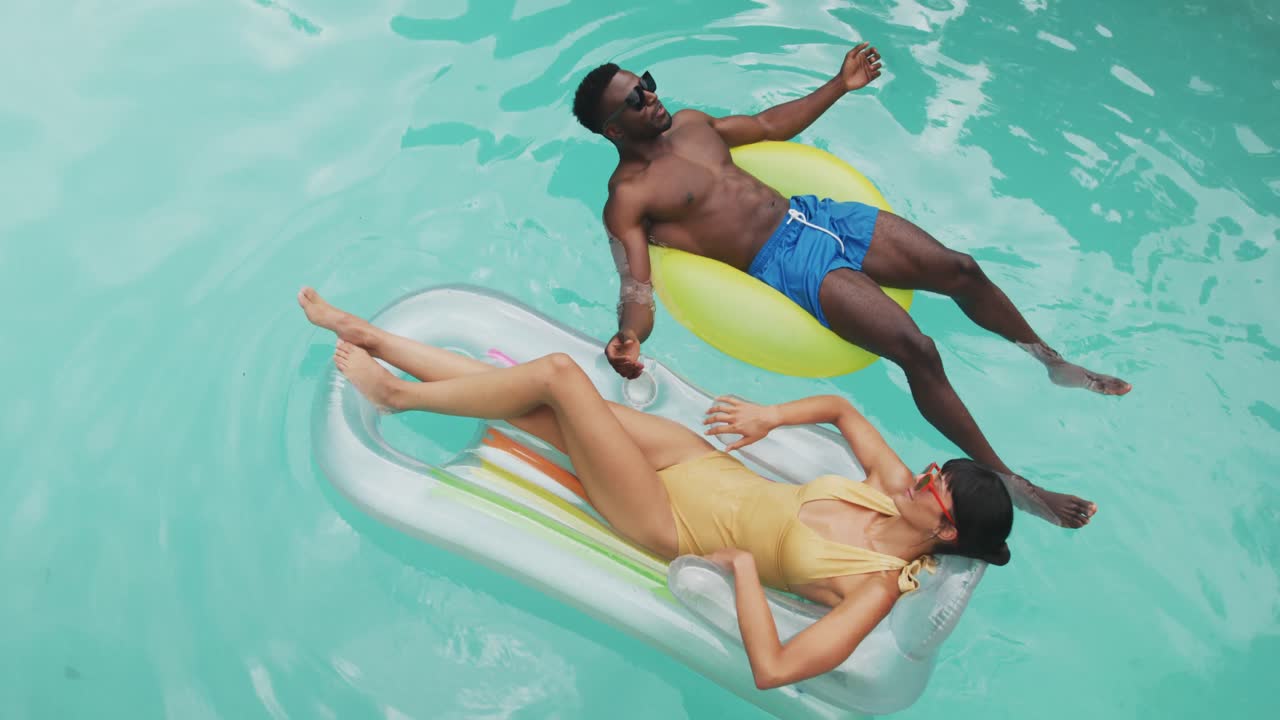 Happy diverse couple wearing swimming suits with inflatables at swimming pool in garden