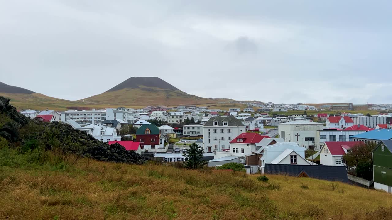 The town of Vestmannaeyjabær with Helgafell volcano in background on cloudy day