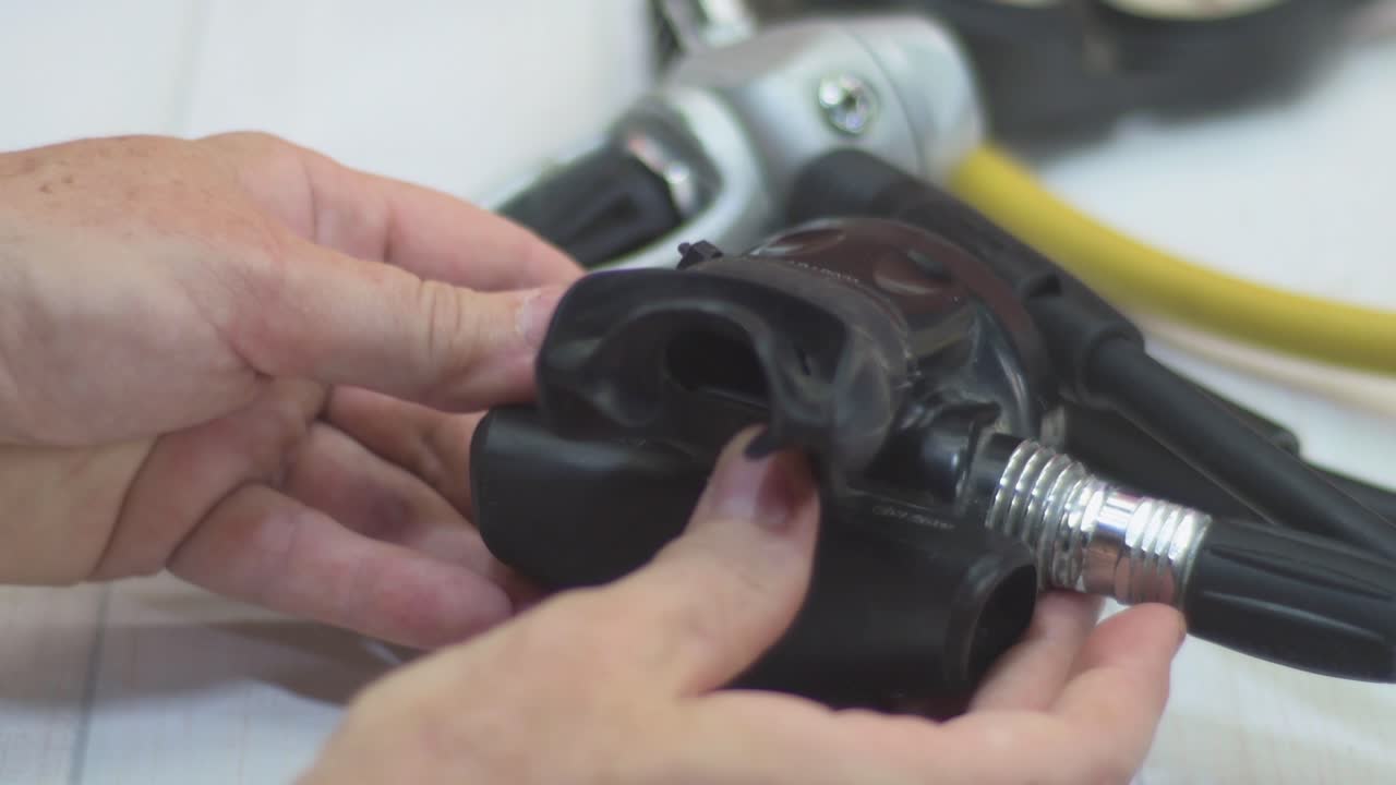 A close-up view showcases a person carefully checking the mouthpiece of scuba gear. This detailed inspection emphasizes the importance of equipment safety for diving enthusiasts