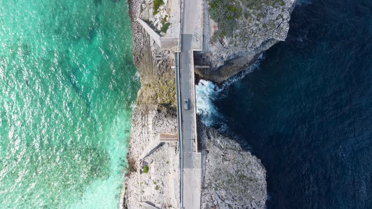 Cinematic aerial view still top down drone shot of a car crossing glass window bridge on the island of eleuthera in the bahamas - separating the atlantic ocean from the caribbean sea