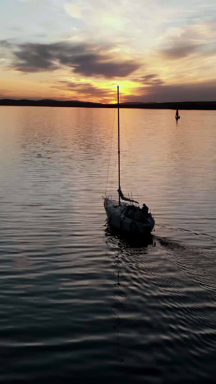 Barca a vela che scivola sull'acqua calma durante un tramonto colorato, riflettendosi sulla superficie tranquilla