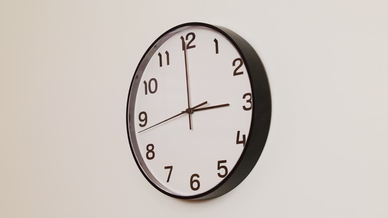 A detailed close-up of a wall clock with a black frame and white face, displaying the time at 3:00.