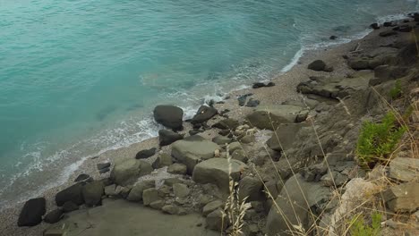 gloomy sea scene with turbid salt water on wild beach with big rocks and pebbles seen from the hill in coastline of mediterranean