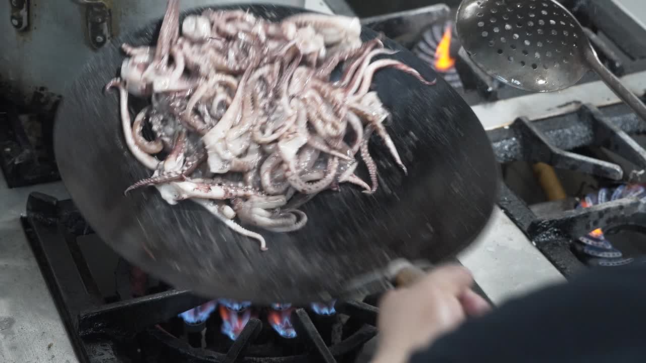 chef lanzando pulpo en un wok sobre una llama alta, acción de cocina