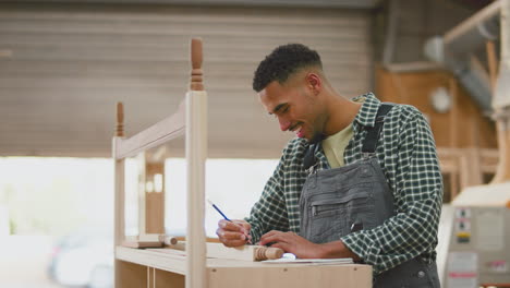 aprendiz masculino que trabaja como carpintero en un taller de muebles haciendo notas