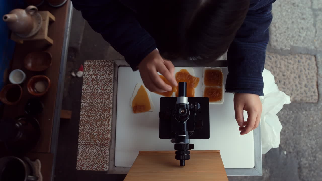 Overhead view of a person using a microscope to examine food samples in an outdoor setting
