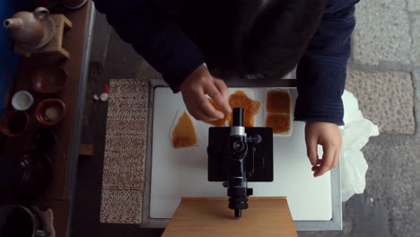 overhead view of a person using a microscope to examine food samples in an outdoor setting