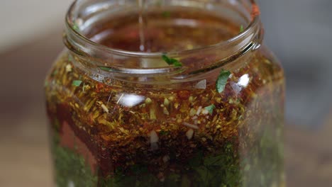 close up video of how the oil is added to a container with ingredients for chimichurri sauce, argentinian cuisine