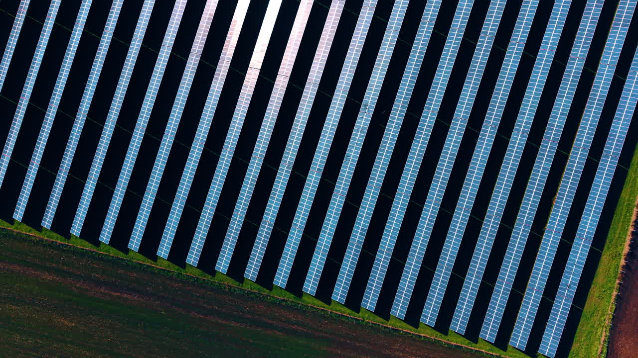 Clip video sopra il campo nero arato e diversi pannelli solari. Produzione di energia verde. Vista aerea