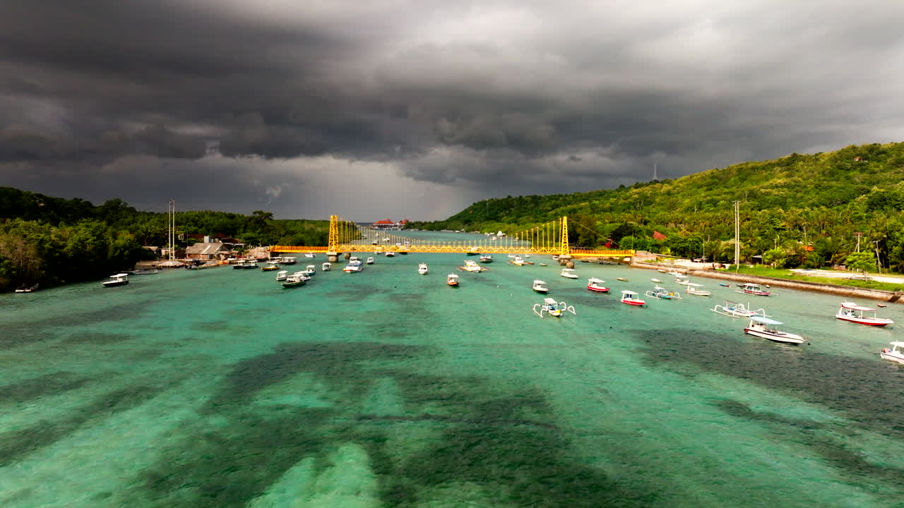 인도네시아의 폭풍 중에 누사 렘본간과 세닌간 섬을 연결하는 노란색 다리와 함께 발리 해의 보트