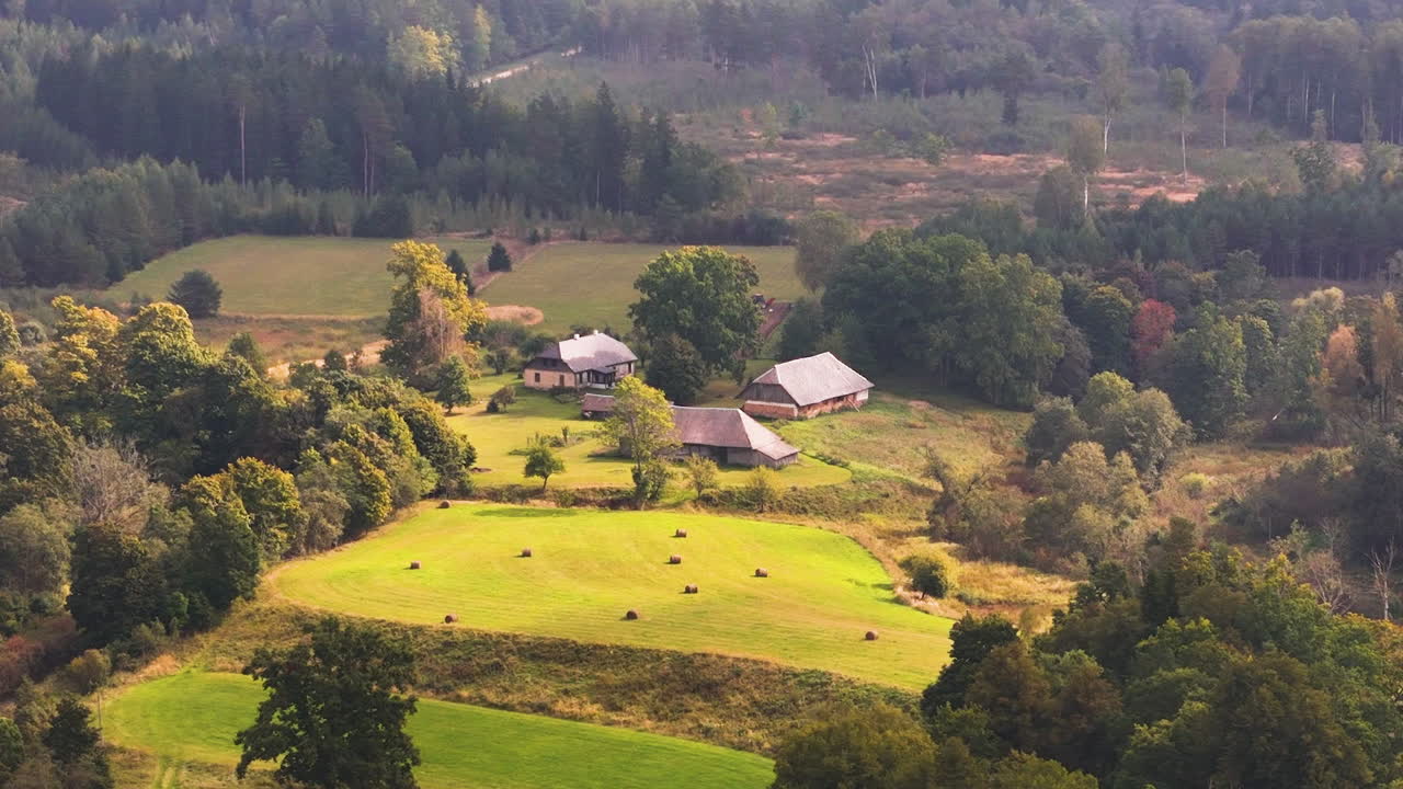Latvian farmland with hay bales and forest edge, captured in a rural deforestation area.
