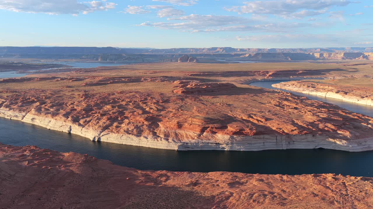 Uma tomada de drone revela uma paisagem de um planeta alienígena de outro mundo. Um rio azul sinuoso flui por monólitos imponentes de arenito e formações geológicas marcantes em um ambiente desértico remoto.