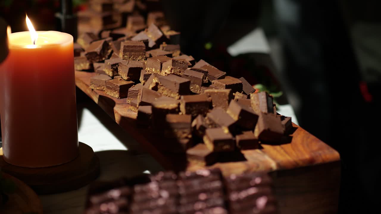 Pieces of dark chocolate arranged on a table beside a softly glowing candle, creating a cozy, elegant and indulgent atmosphere, ideal for relaxation or gourmet themes.