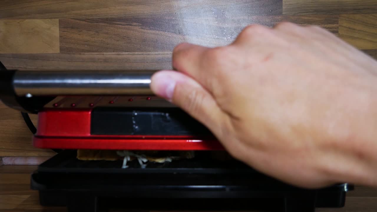 Pressing down a sandwich maker machine to cook sandwiches inside for dinner in household