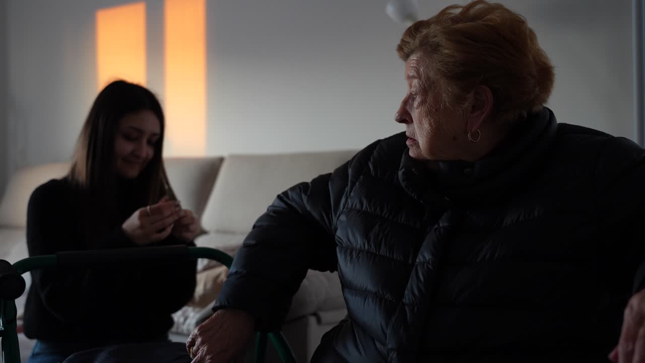 Grandmother chats with granddaughter indoors wearing a coat ready to go outdoors