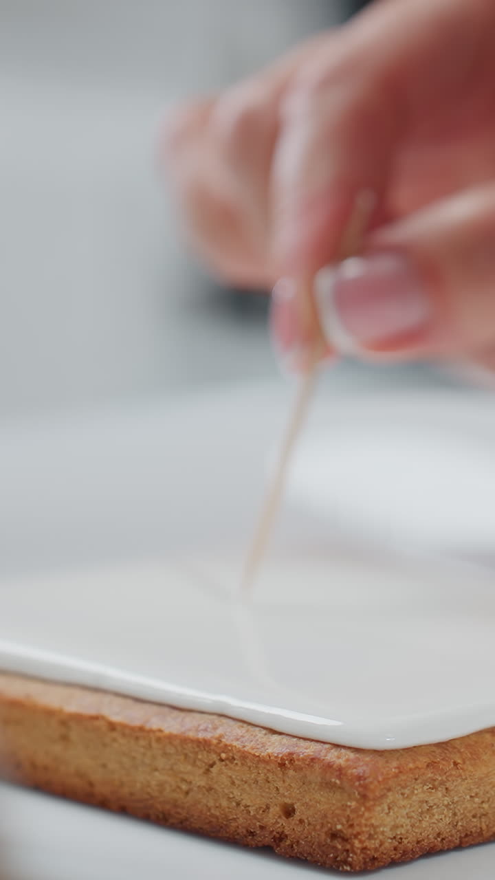 색 세라 접시 위에 놓인 쿠키에 완벽한 아이싱을 위해 을 사용하는 베이커의 클로즈업, 부드러운 색 아이싱이 정밀하게 조정됩니다.